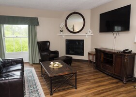 Una sala de estar con sofá de cuero, una mesa de centro con objetos decorativos, chimenea, televisor y una ventana grande con cortinas.