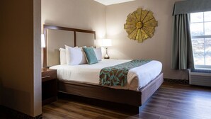 A hotel room with a large bed, a nightstand, a wall-mounted lamp, and a decorative sunburst wall art piece.