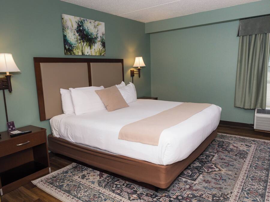 A hotel room with a large bed, two bedside lamps, a nightstand, a wall-mounted air conditioner, and a window with curtains.