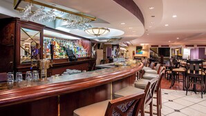 Zona de bar con mostrador de madera, taburetes y una variedad de botellas y vasos.