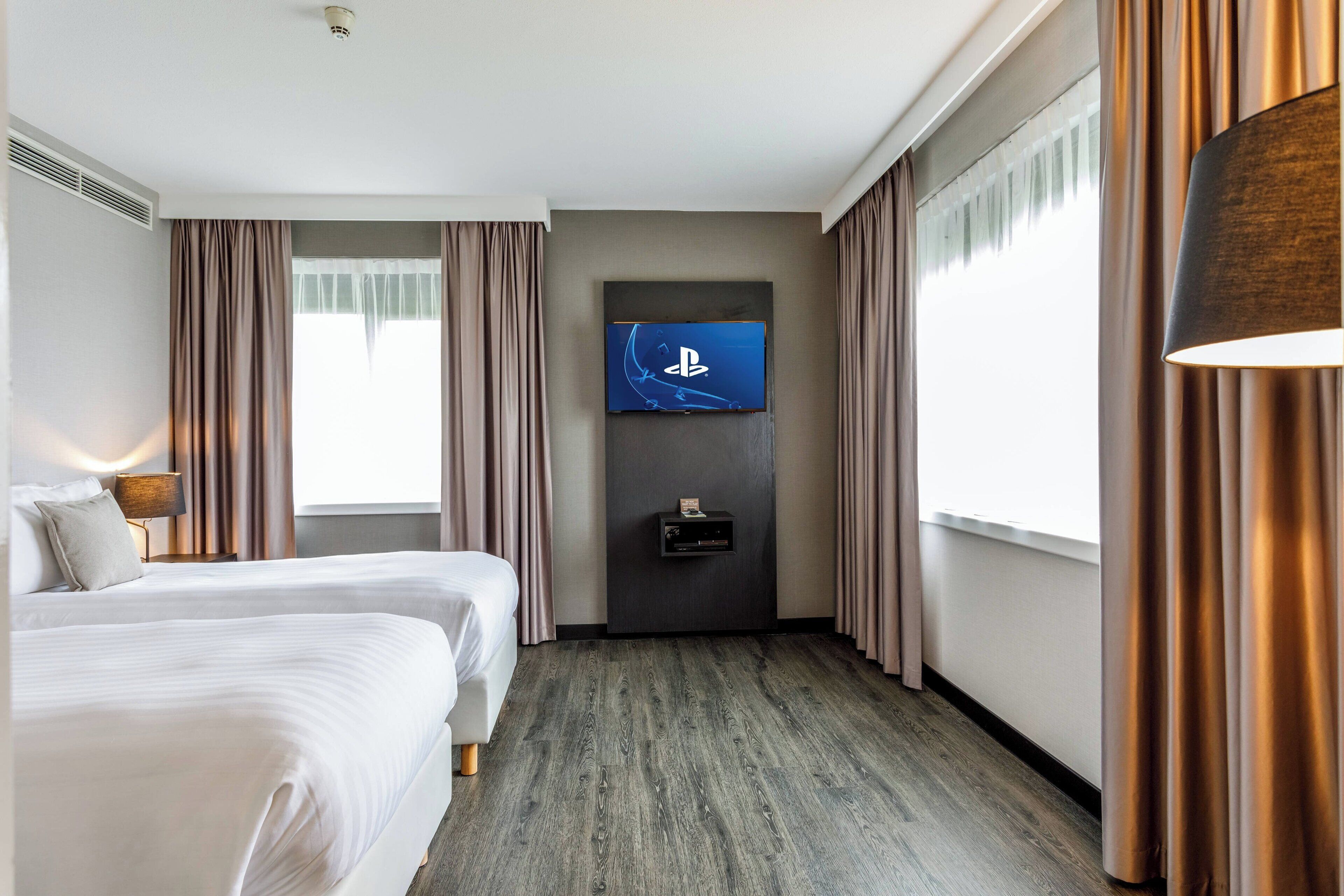 A hotel room with a large bed, a flat-screen TV mounted on the wall, and a small table with a lamp.
