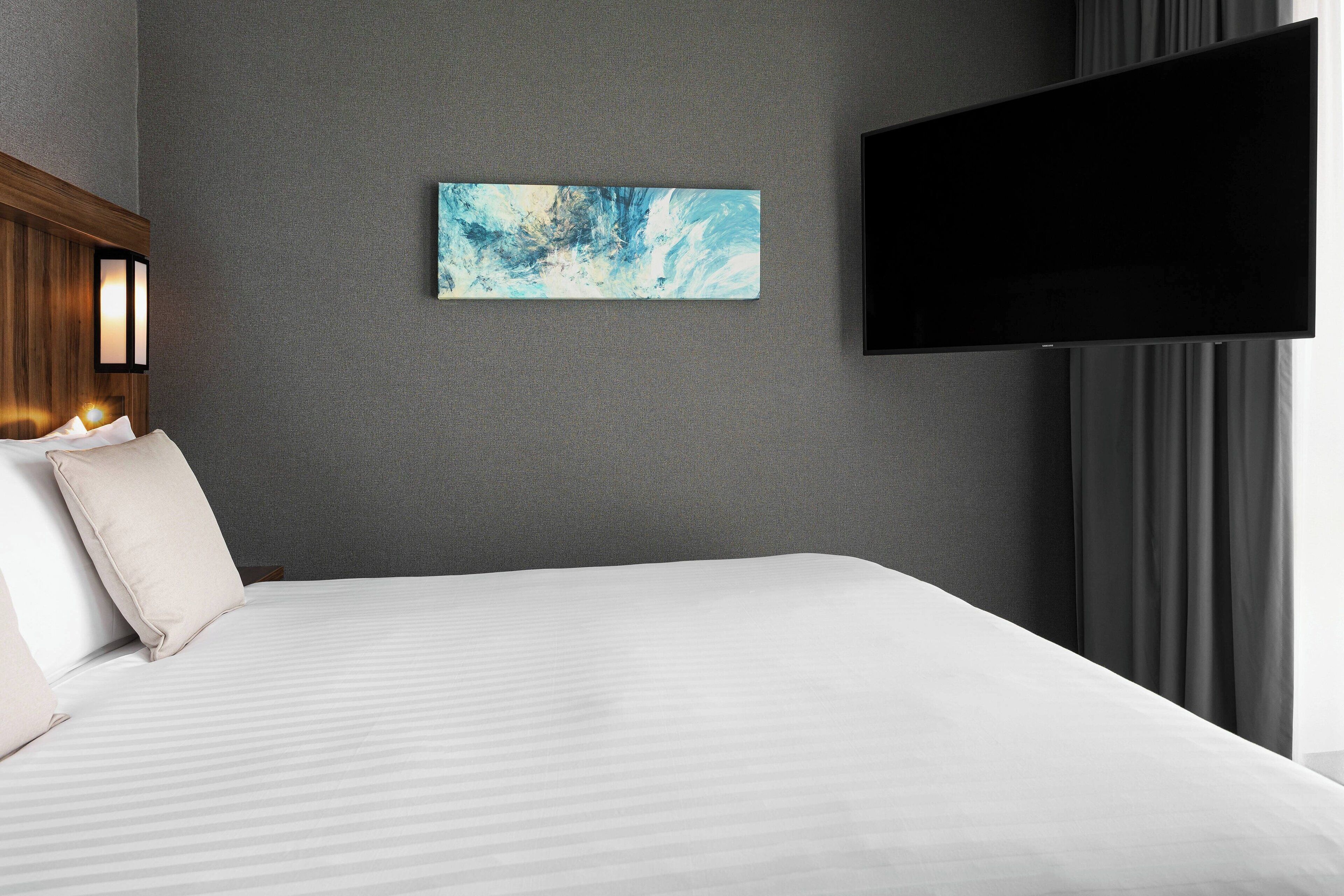 A hotel room with a bed, a flat-screen TV mounted on the wall, and a painting above the bed.
