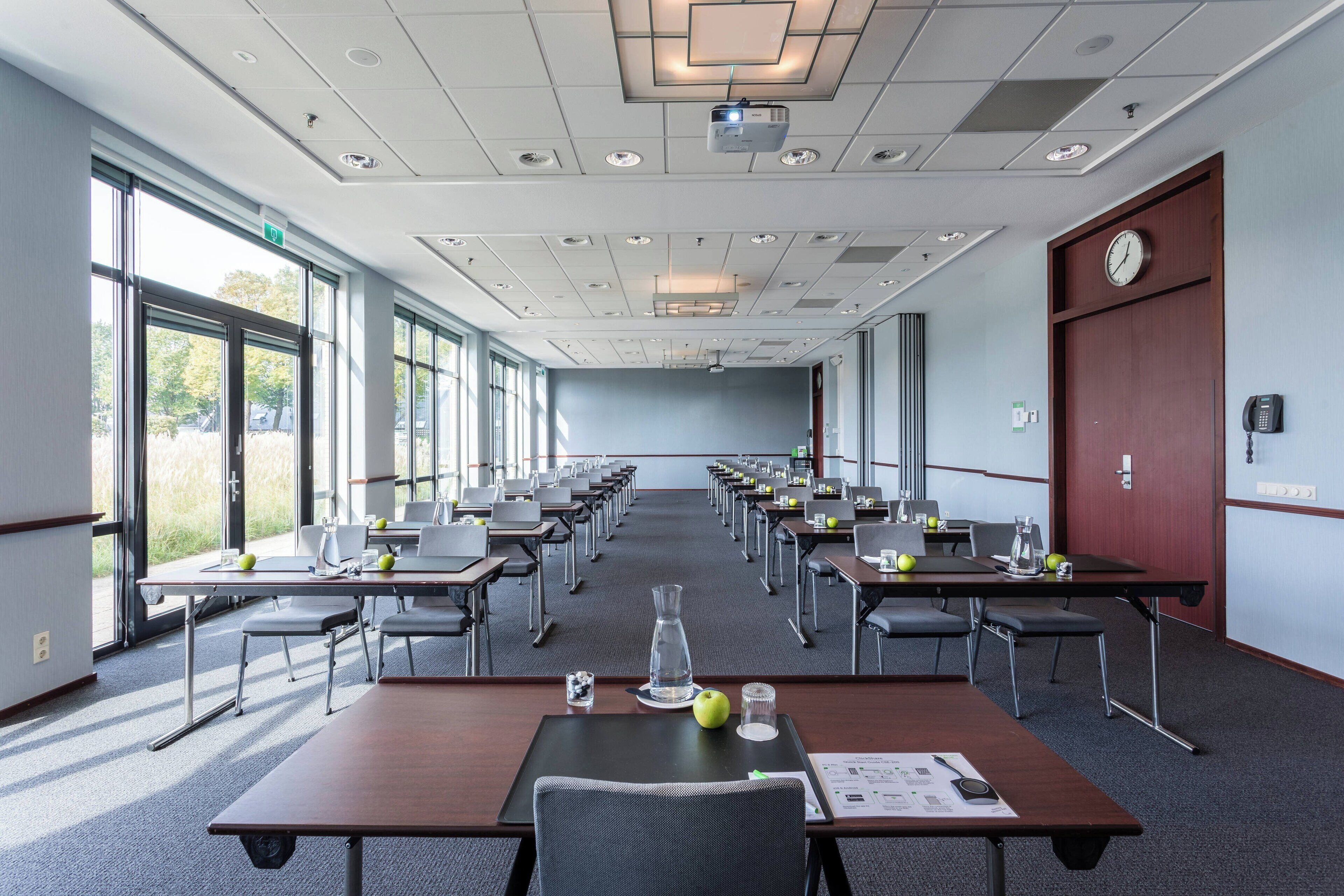 A conference room with multiple tables, chairs, and a projector screen.