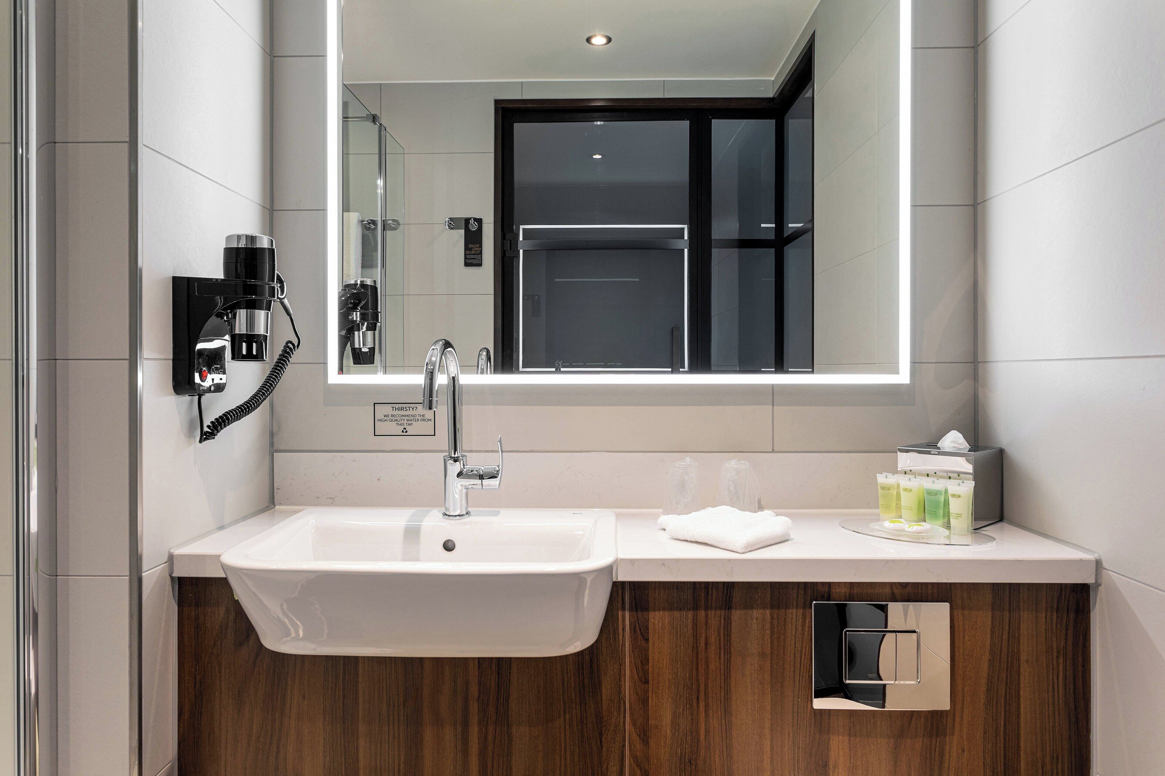 A modern bathroom with a white sink, a mirror, a hairdryer, and a towel rack.