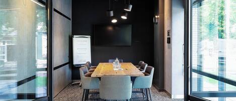 A conference room with a large table, six chairs, a TV screen, and a welcome sign.