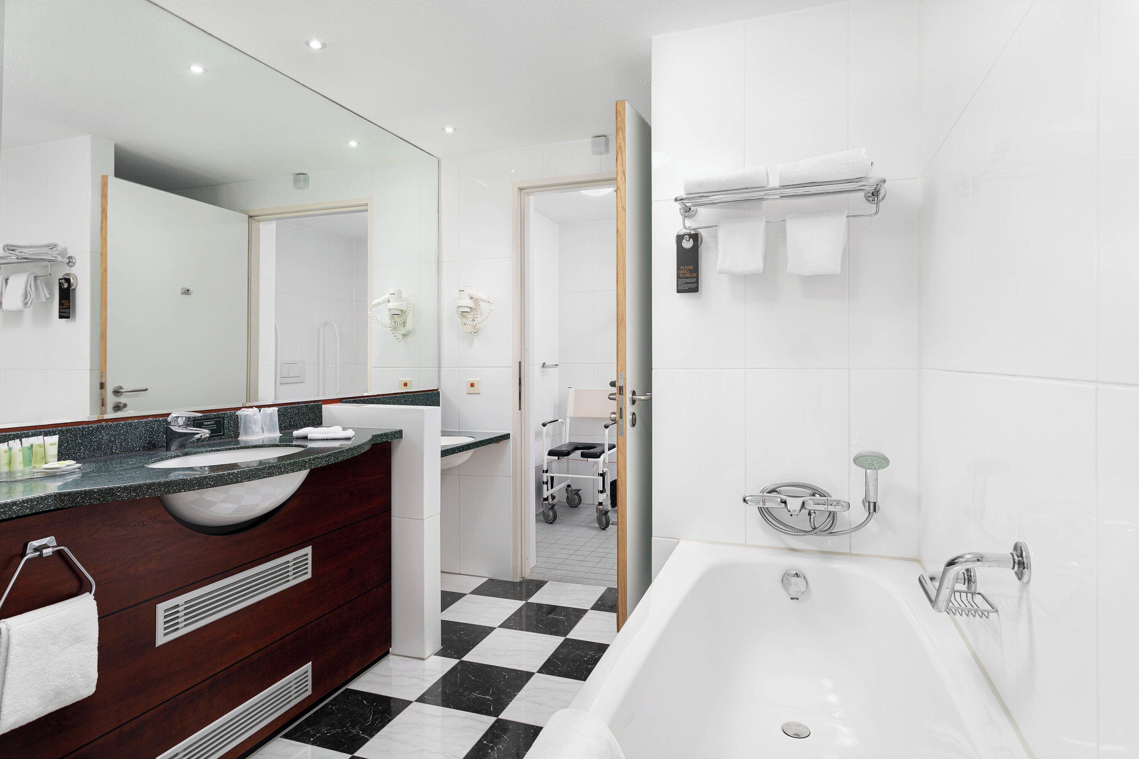 A modern bathroom with a large mirror, two sinks, a bathtub, and a shower area.