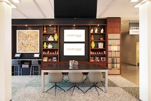 A meeting room with a long table, three chairs, a bookshelf with decorative items, and a large abstract painting. - Courtyard by Marriott Amsterdam Airport (Hoofddorp)