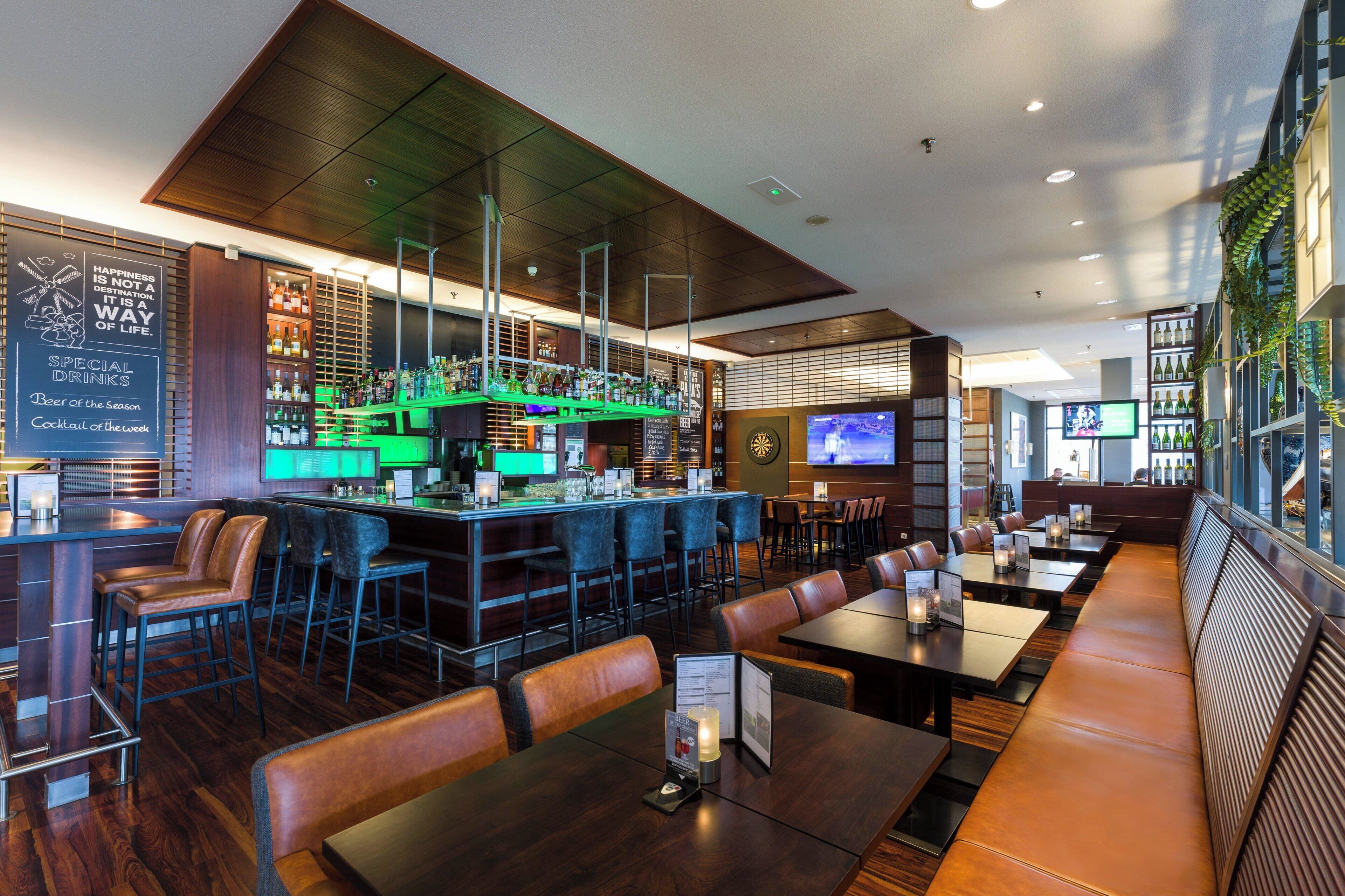 A modern bar area with a counter, seating, and a television screen.