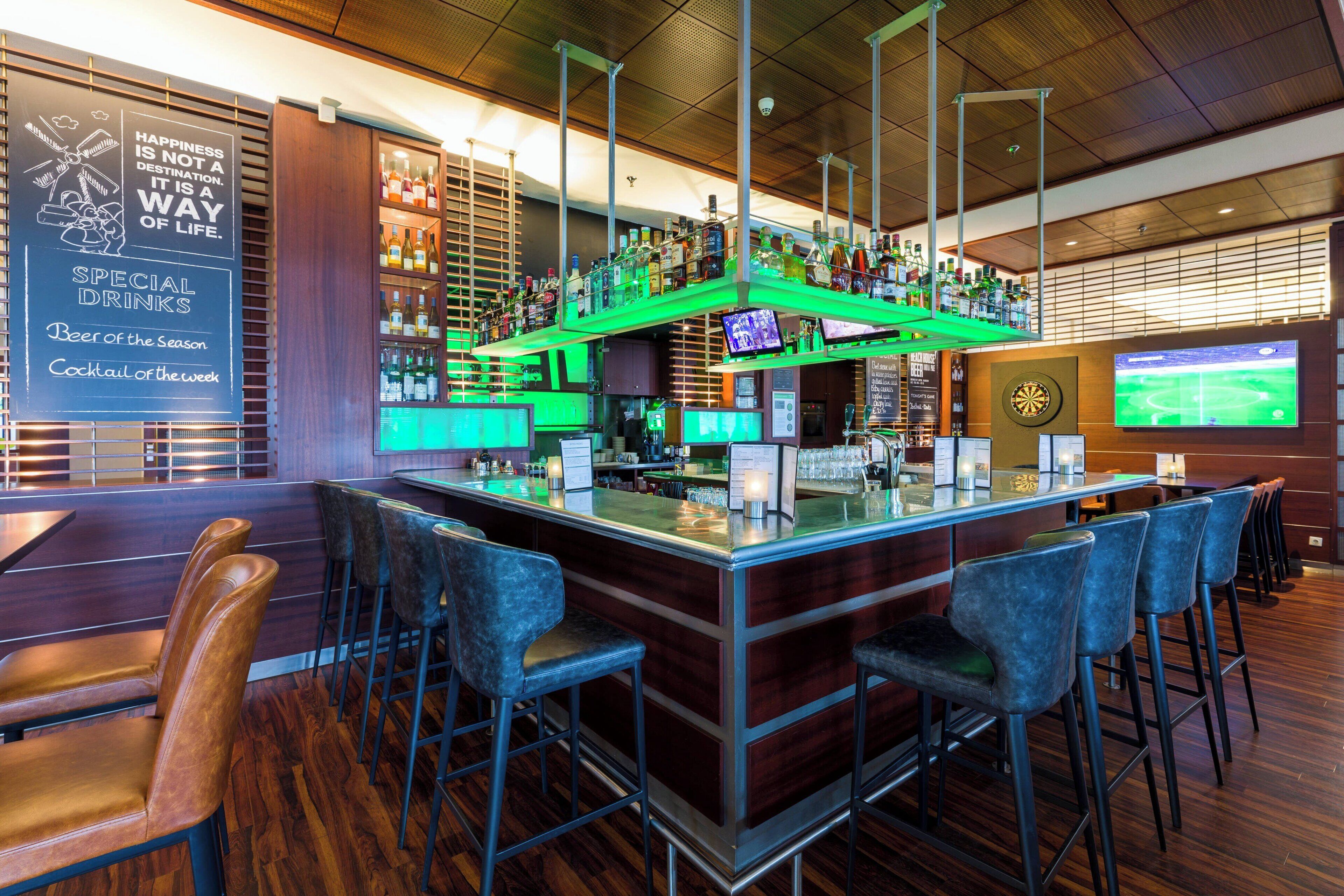 A bar area with a high counter, stools, and a television screen displaying a sports game.