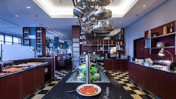 Un área de bufé con piso a cuadros, una estación de servicio central y diversos alimentos exhibidos en estanterías.