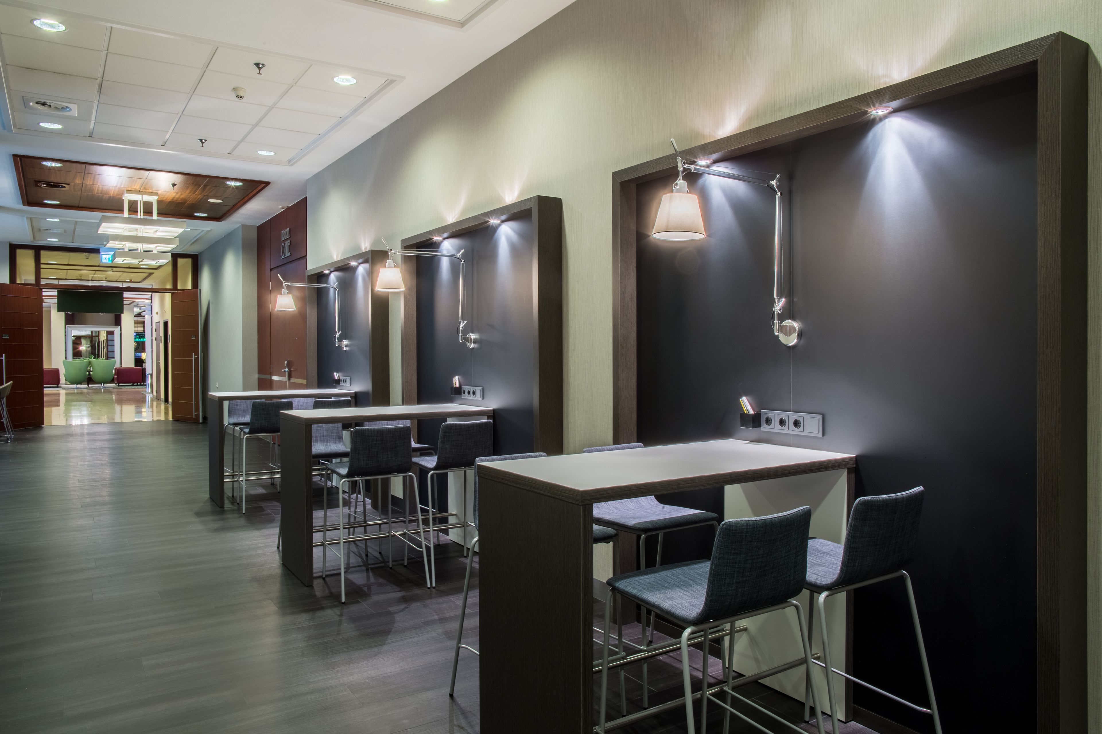 A modern restroom with multiple sinks, each with a mirror and a light fixture. There are several chairs and tables arranged in the area.