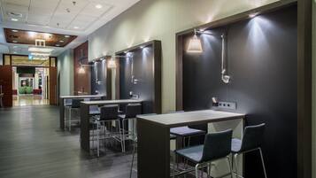 Een moderne toiletruimte met meerdere wastafels, elk met een spiegel en een lamp. Er staan verschillende stoelen en tafels in de ruimte.
