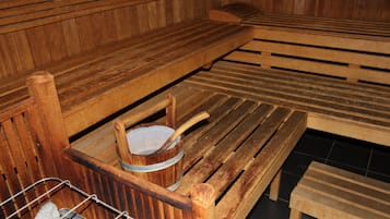 Un sauna en bois, doté de bancs et d’une étagère en métal où sont disposées des pierres.