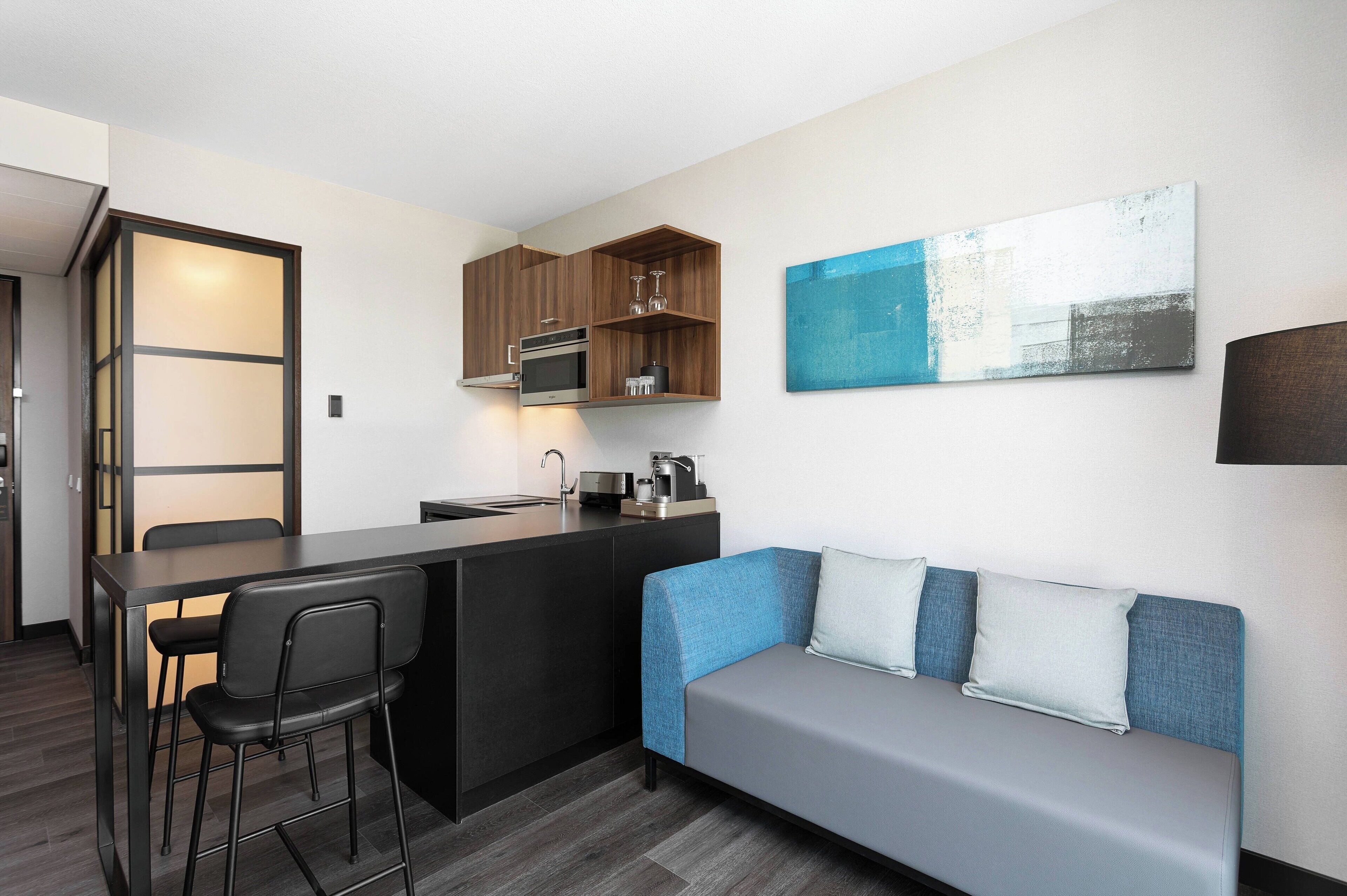 Una cocina moderna con una isla central, taburetes de bar y un sofá con cojines.