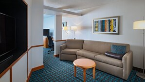 A hotel room with a sofa, a small round table, a TV, a lamp, and a framed picture on the wall. - Fairfield Inn & Suites by Marriott McAllen Airport (McAllen)
