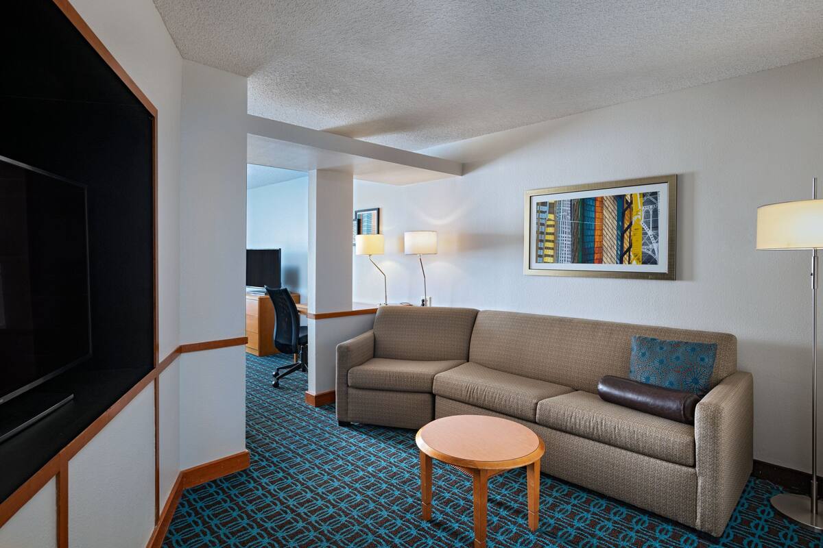 Une chambre d’hôtel avec un canapé, une petite table ronde, un téléviseur, une lampe et un tableau encadré au mur.