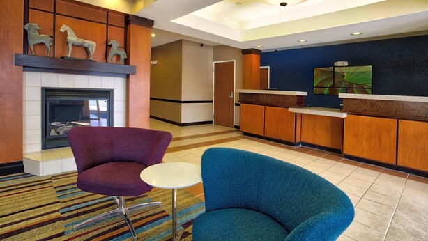 A hotel lobby with a fireplace, two armchairs, a small table, a reception desk, and a painting on the wall. - Fairfield Inn & Suites by Marriott McAllen Airport (McAllen)