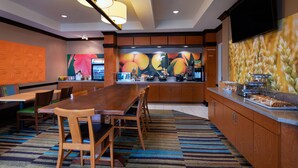 A modern hotel room with a large wooden dining table, comfortable seating, a kitchen area with a microwave, and a large flat-screen TV mounted on the wall. - Fairfield Inn & Suites by Marriott McAllen Airport (McAllen)
