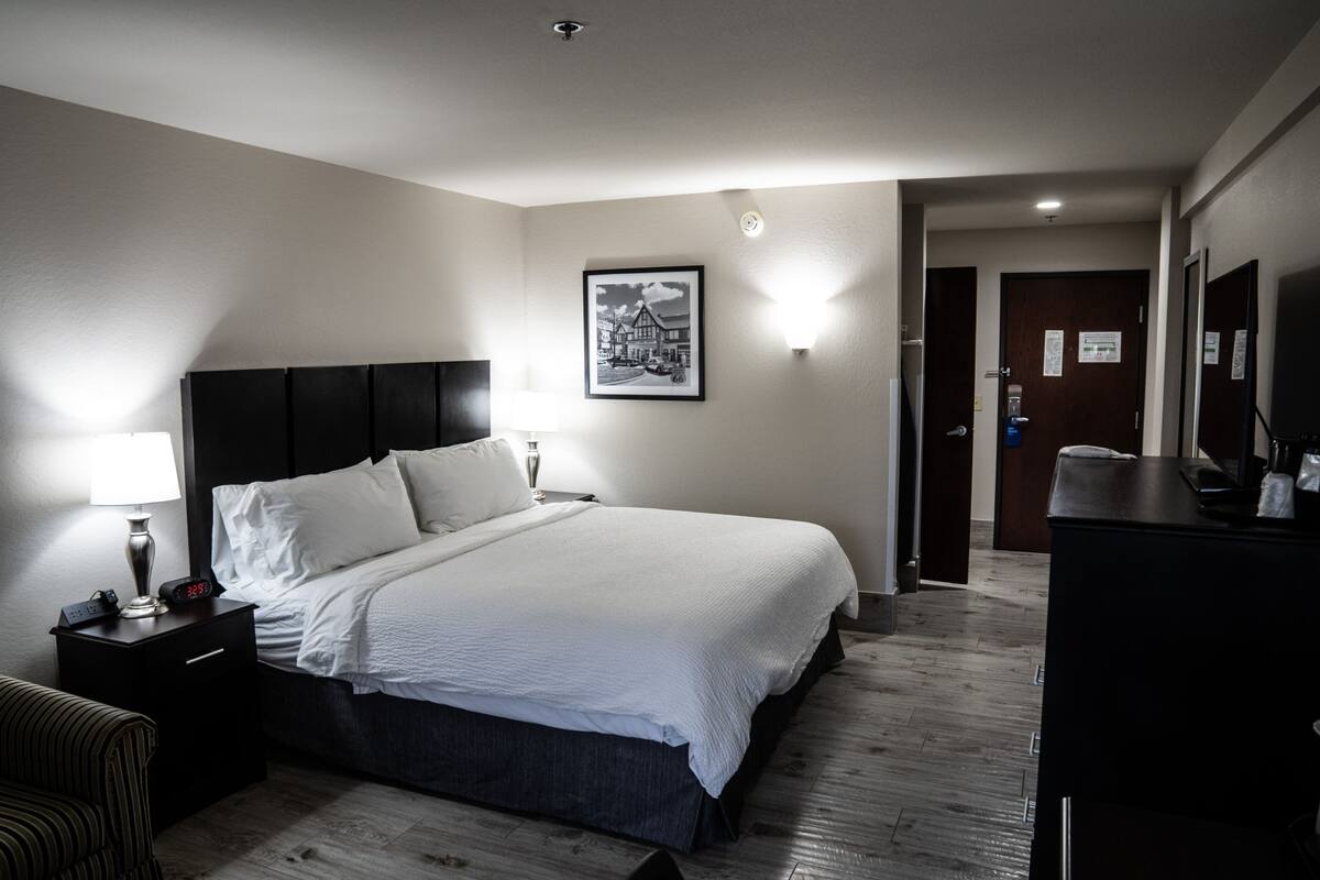 Una habitación de hotel con una cama grande, mesitas de noche, una lámpara, un cuadro en la pared y un escritorio con un espejo.