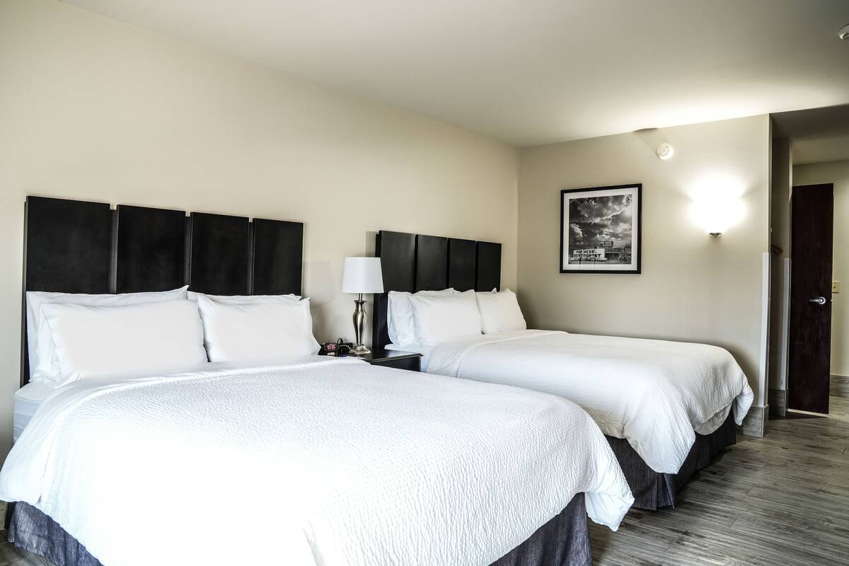 Habitación de hotel con dos camas, una mesita de noche, una lámpara y un cuadro en la pared.