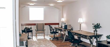 A modern office space with a wooden desk, two chairs, a sofa, and a small table with a lamp and plant.