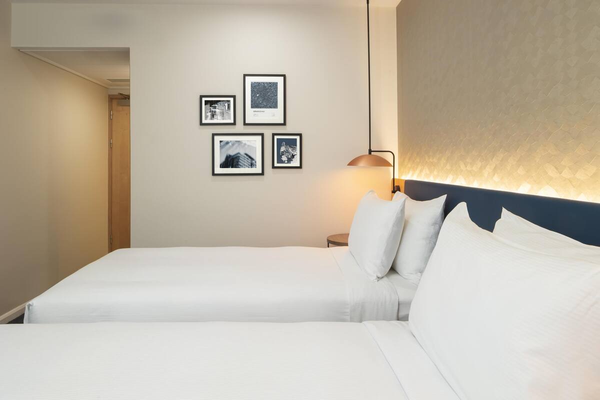 Une chambre d’hôtel avec un grand lit, une table de chevet, une lampe et quatre tableaux encadrés au mur.