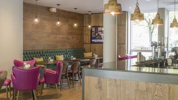 A restaurant with wooden walls, green cushioned seating, and pendant lighting.