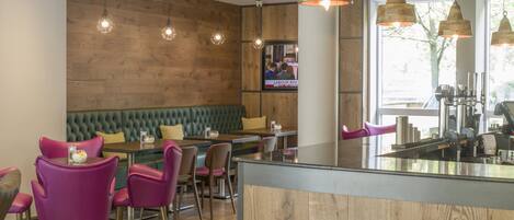 A restaurant with wooden walls, green cushioned seating, and pendant lighting.