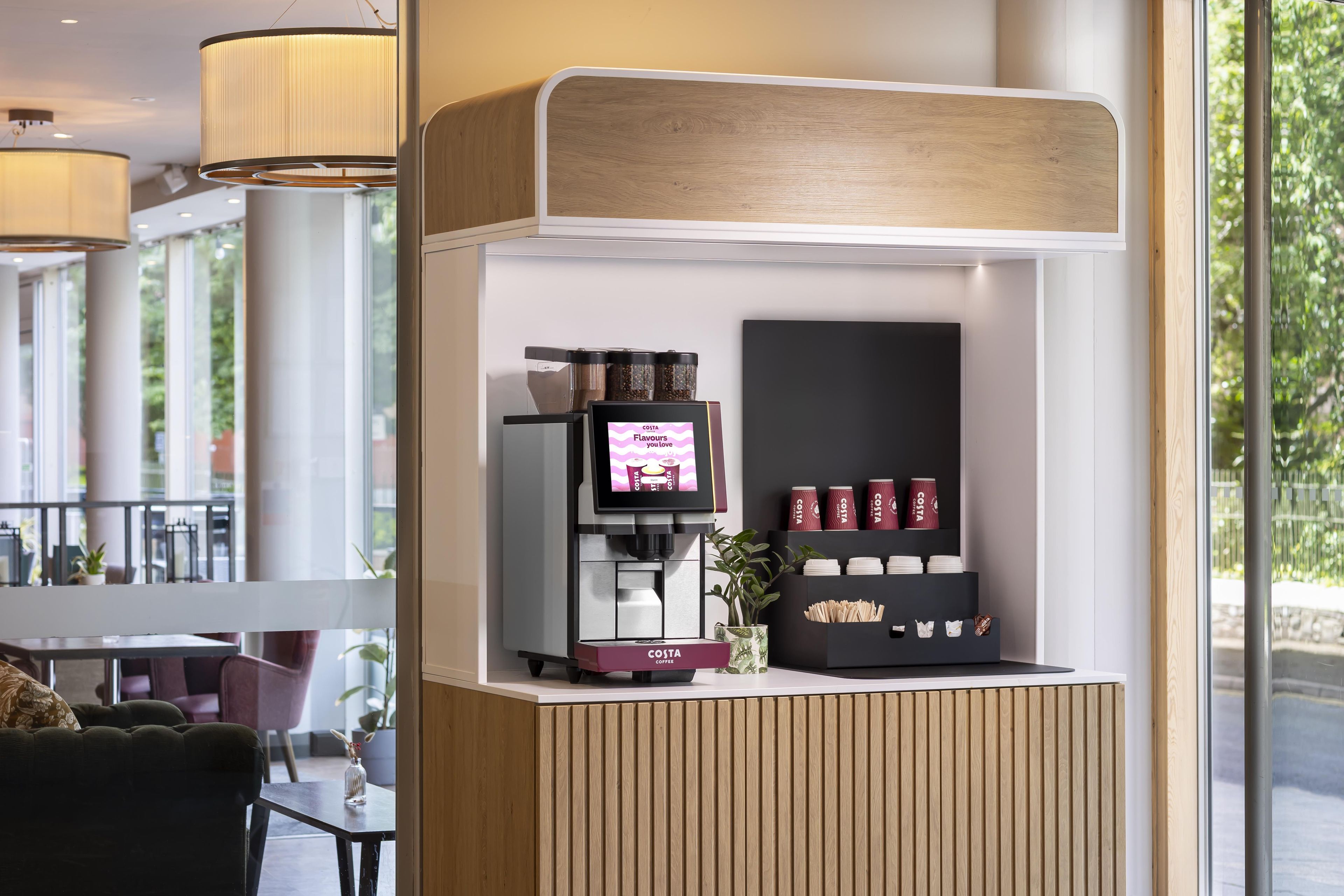 Costa Coffee -myymälän osa, jossa on digitaalinen valikko, kahviautomaatit ja valikoima brändättyjä kuppeja.