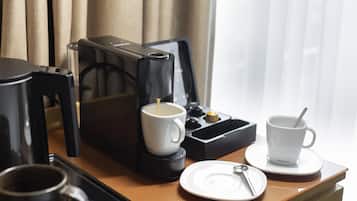 A hotel room with a coffee maker, two white cups, a plate with a spoon, and a key on a wooden table.