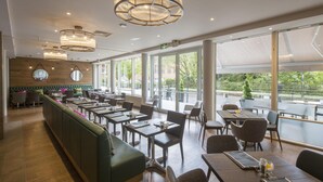 A spacious restaurant with high ceilings, large windows, and modern lighting fixtures. - Hilton Garden Inn Bristol City Centre (Bristol)
