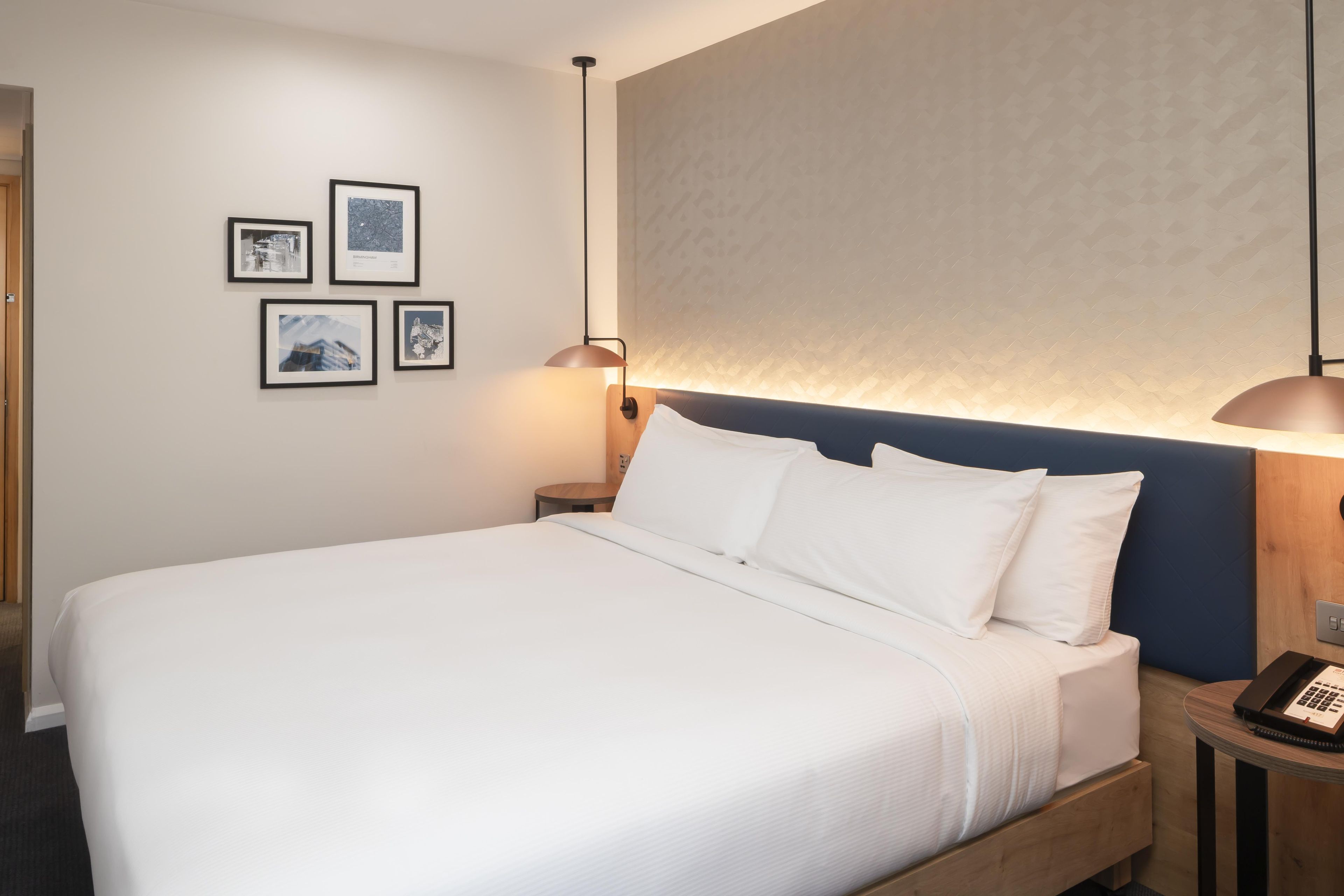 Een hotelkamer met een groot bed, een nachtkastje met een lamp en een telefoon aan de muur.