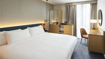 A hotel room with a large bed, a desk with a chair, a mirror, and a wardrobe.