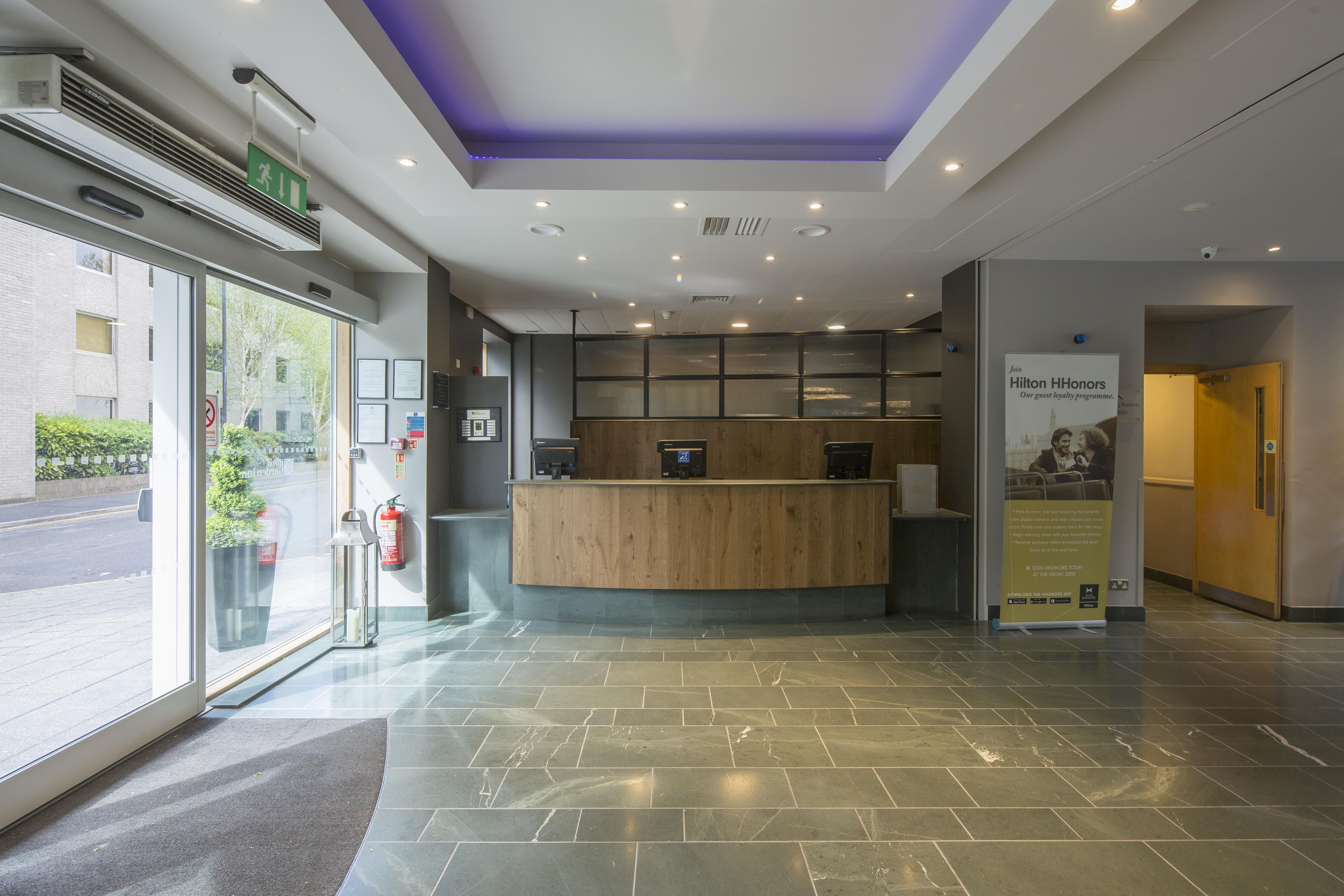 A reception area with a wooden counter, a fire extinguisher, and a sign promoting Hilton HHonors.