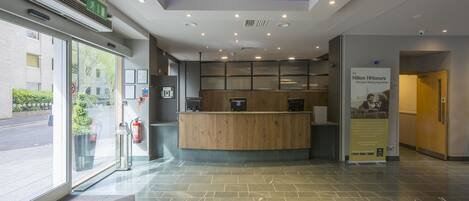 A reception area with a wooden counter, a fire extinguisher, and a sign promoting Hilton HHonors.