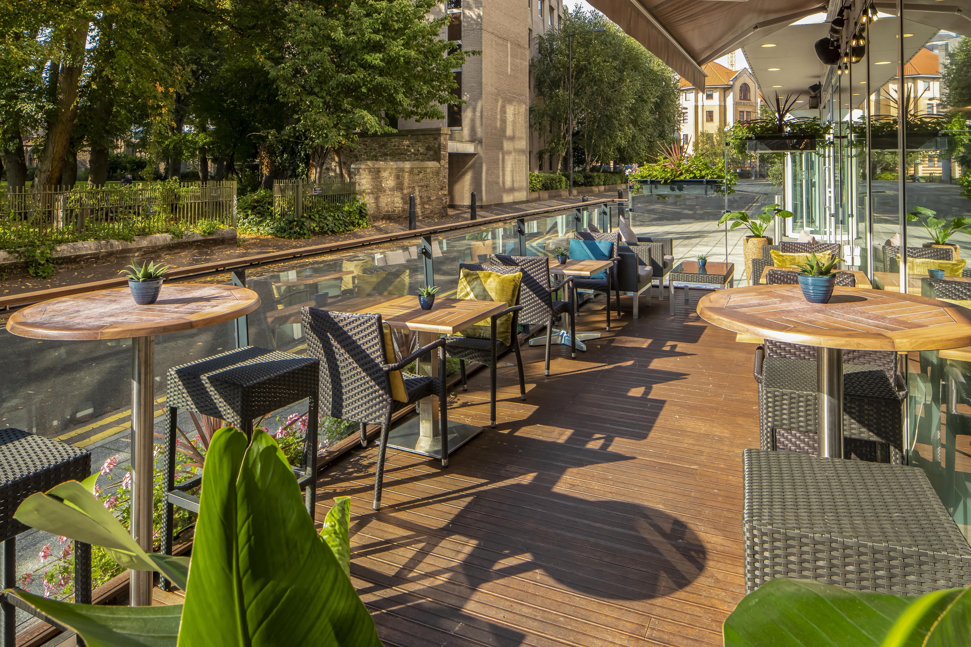 An outdoor terrace with wicker furniture and glass railings, overlooking a street.