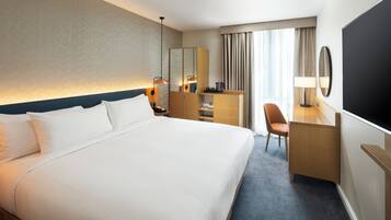 A hotel room with a large bed, a desk, a chair, a TV, and a window with curtains.
