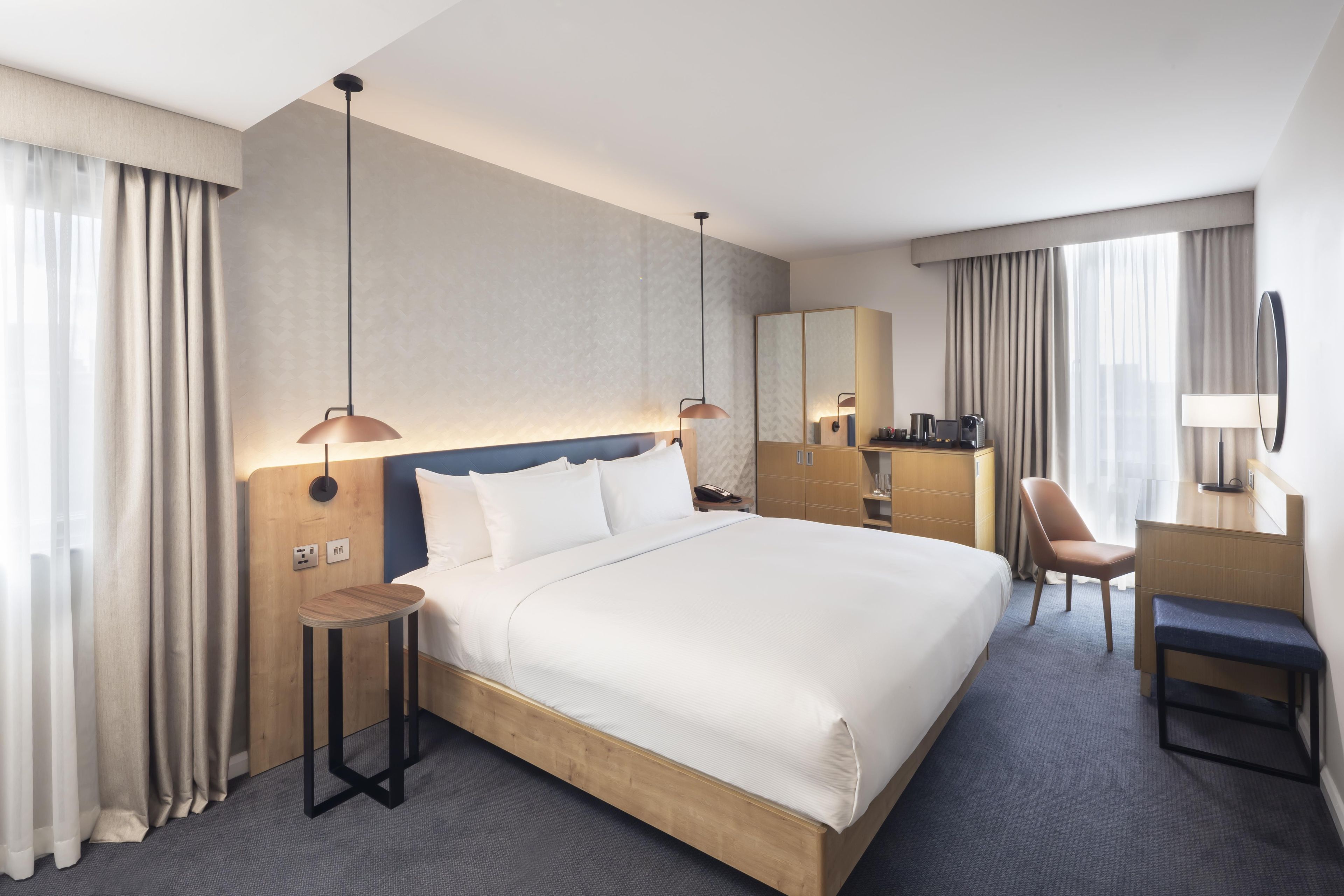 A hotel room with a large bed, bedside lamps, a desk, a chair, and a mirror.