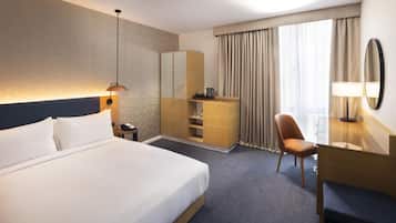 A hotel room with a large bed, a desk, a chair, a wardrobe, and a mirror.