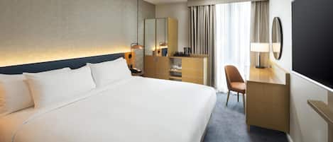 A hotel room with a large bed, a desk, a chair, a TV, and a window with curtains.