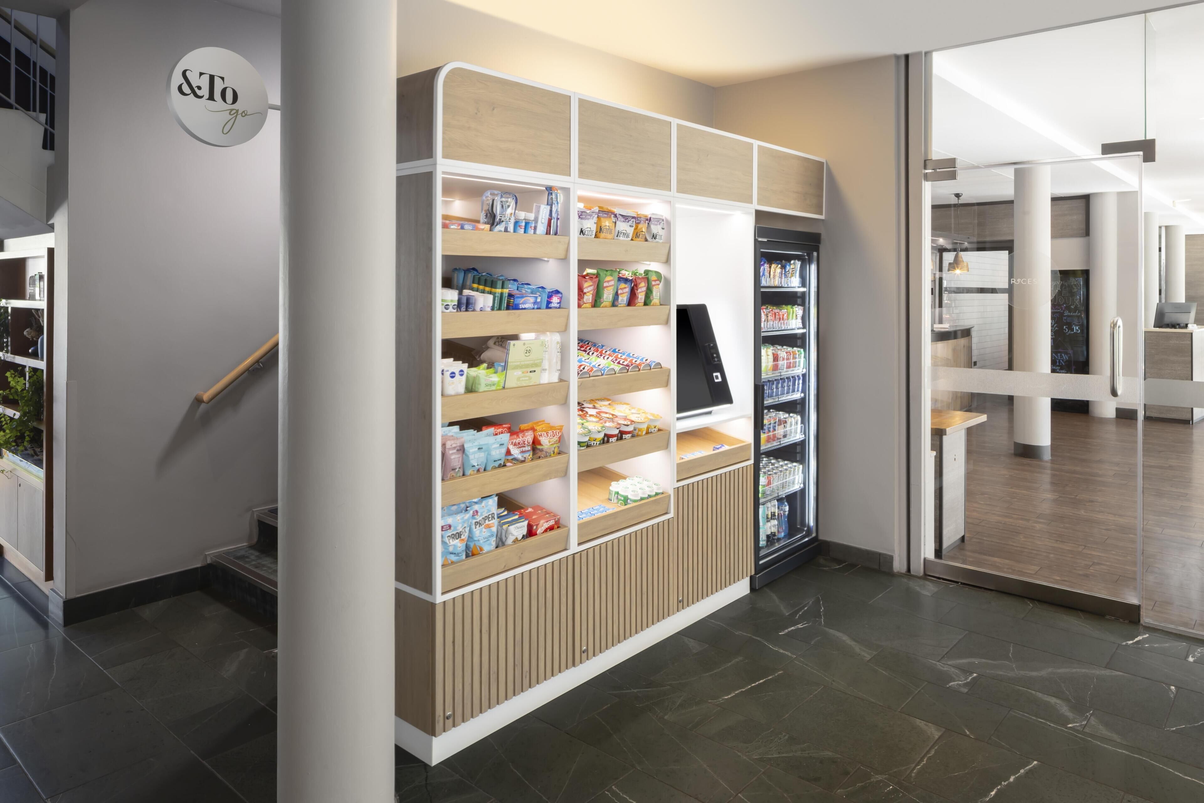 A modern retail area with shelves stocked with various products, a digital kiosk, and a refrigerator.