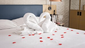 A neatly made bed with white towels arranged in a heart shape, a bottle of champagne, and glasses on a bedside table. - Hilton Garden Inn Bristol City Centre (Bristol)