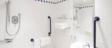 A modern bathroom with white tiles, a sink, a shower, and grab bars.