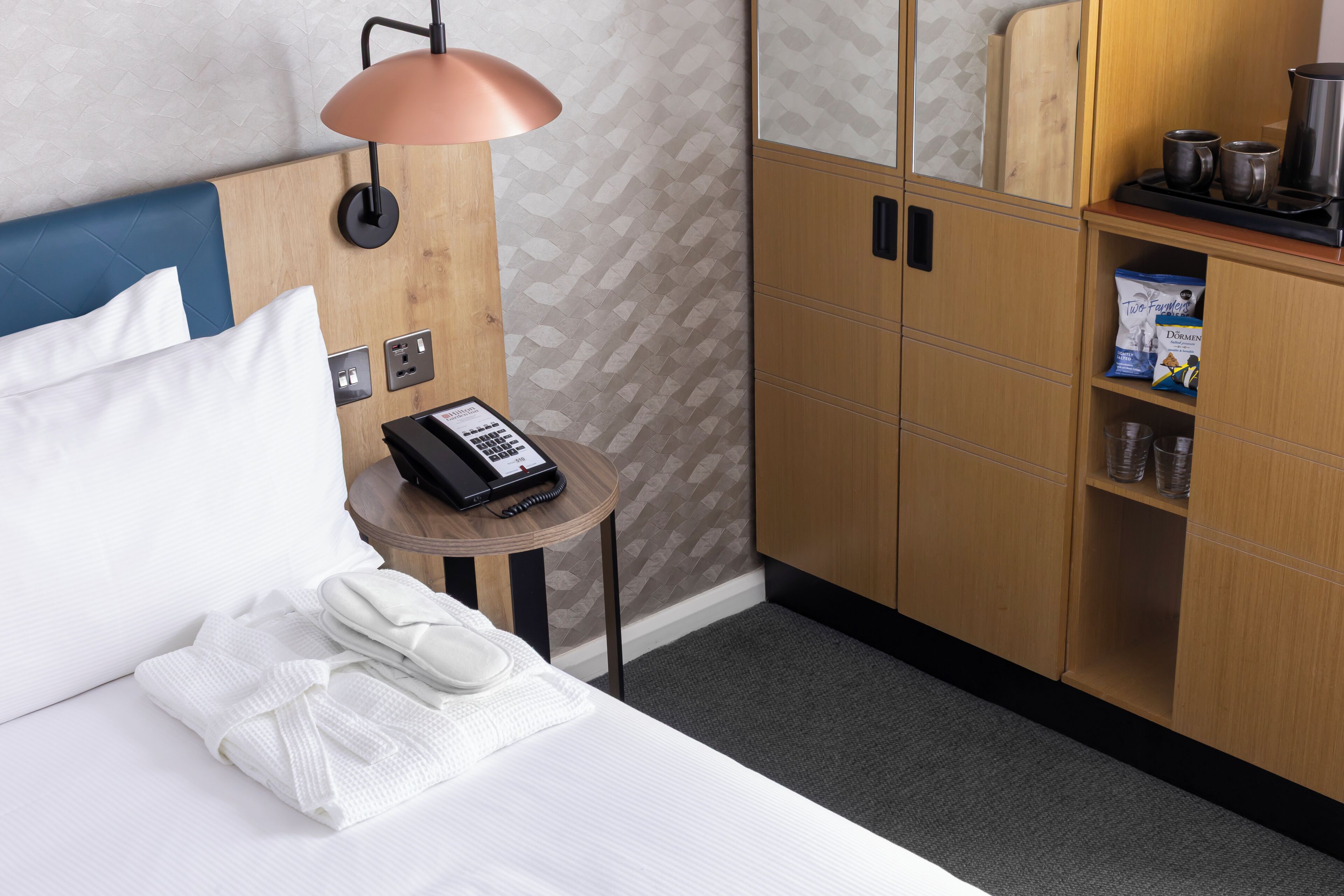 Une chambre d’hôtel comprenant un lit, une table de chevet avec une lampe, un téléphone et un mini-bar.