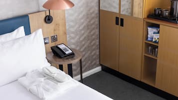 Une chambre d’hôtel comprenant un lit, une table de chevet avec une lampe, un téléphone et un mini-bar.