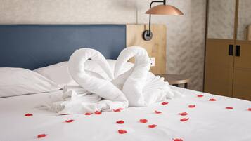 A neatly made bed with white linens, a blue headboard, and a wooden nightstand with a lamp.
