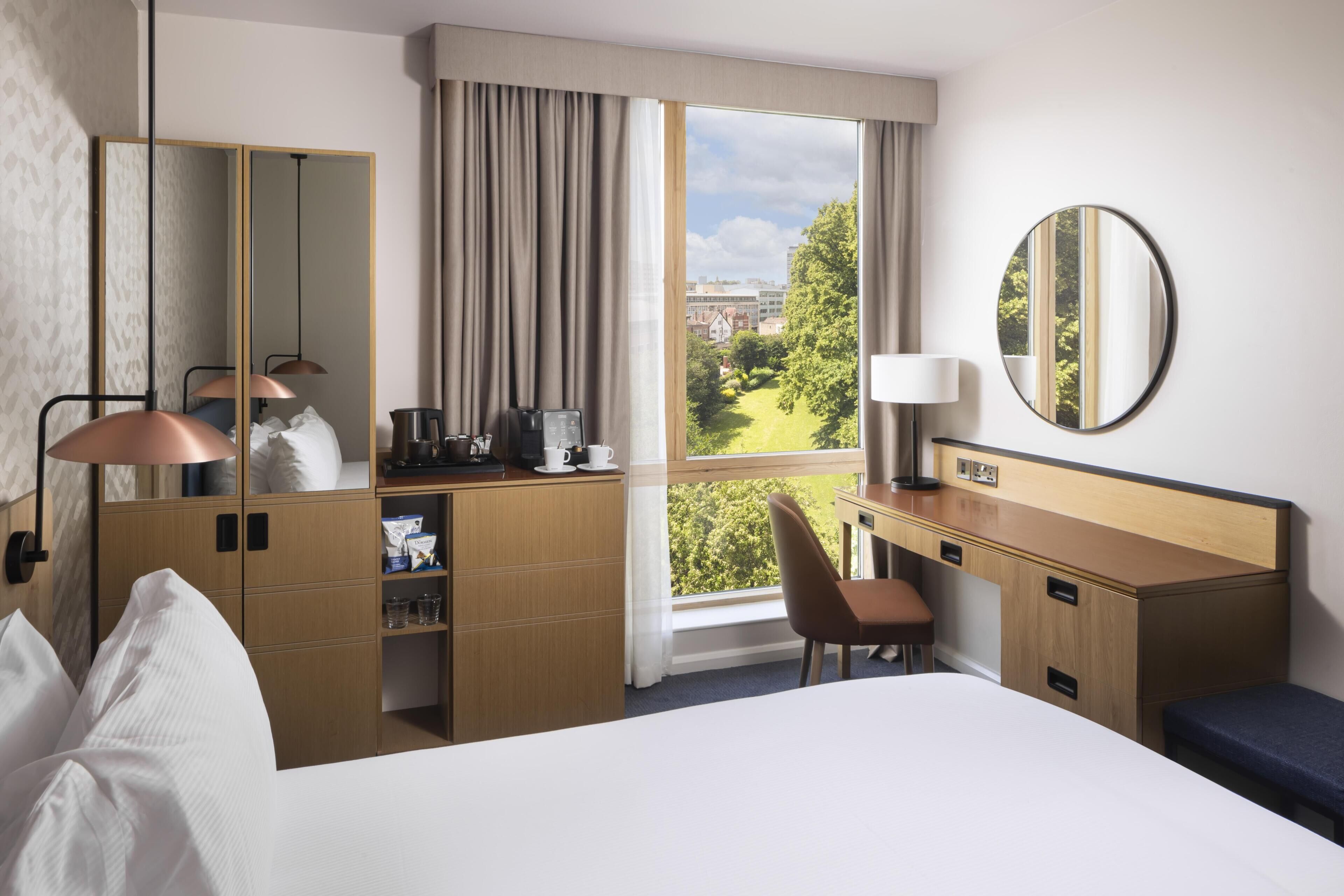 Hotelkamer met een bed, bureau, stoel, spiegel, raam met uitzicht en een kledingkast.