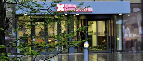 A hotel entrance with a visible sign, glass doors, and a tree in the foreground.