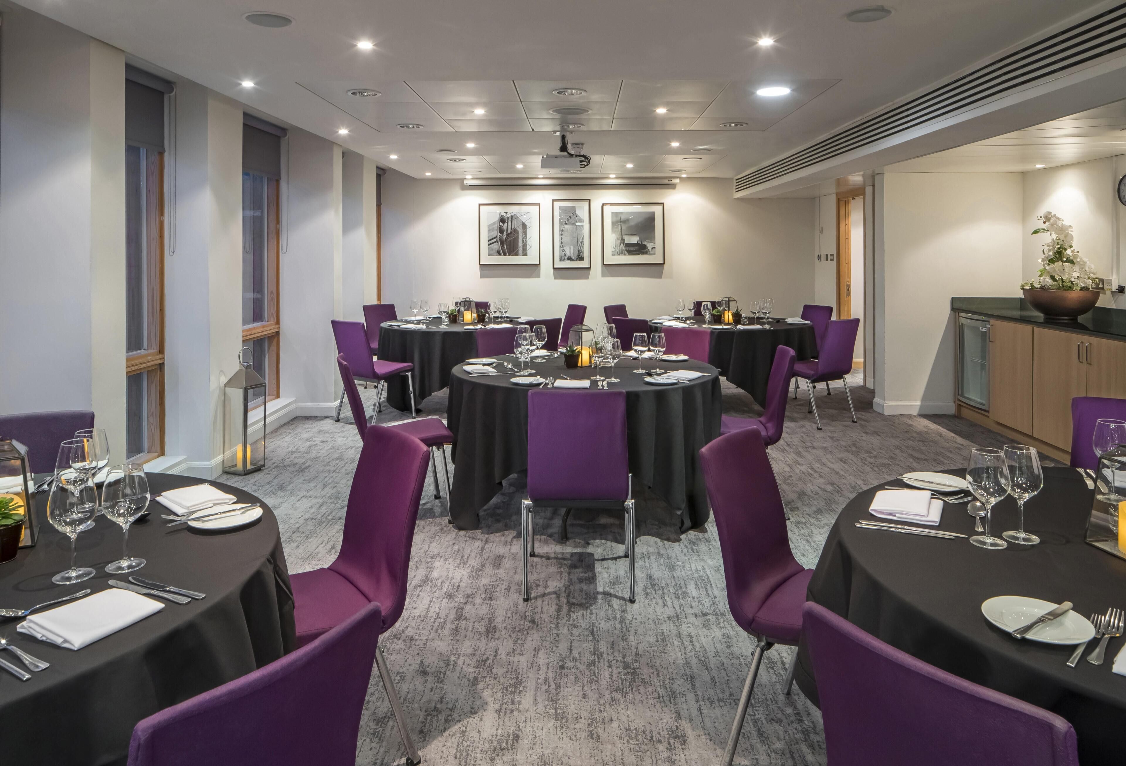 Une salle de conférence avec des tables rondes, des chaises violettes et des nappes noires.