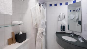 A bathroom with a glass shower enclosure, a white bathtub, a vanity with a dark countertop, and a mirror.